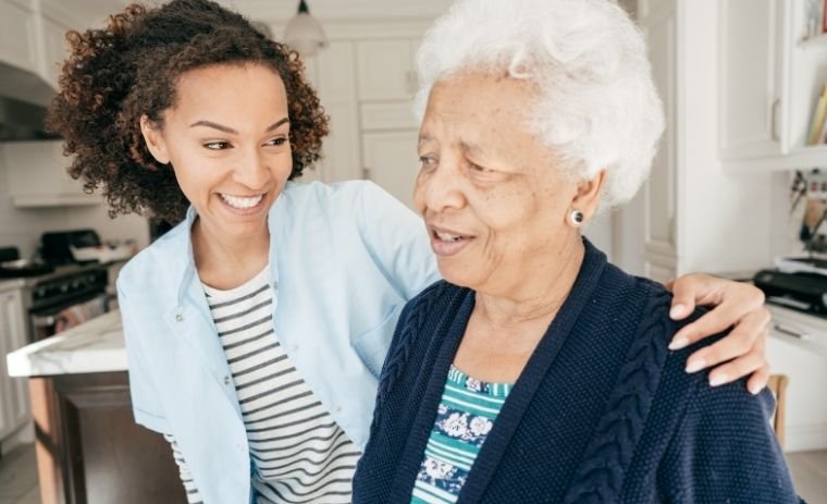 A smiling caregiver supporting an elderly woman in a bright kitchen, symbolizing independence and comfort through home health care in Michigan