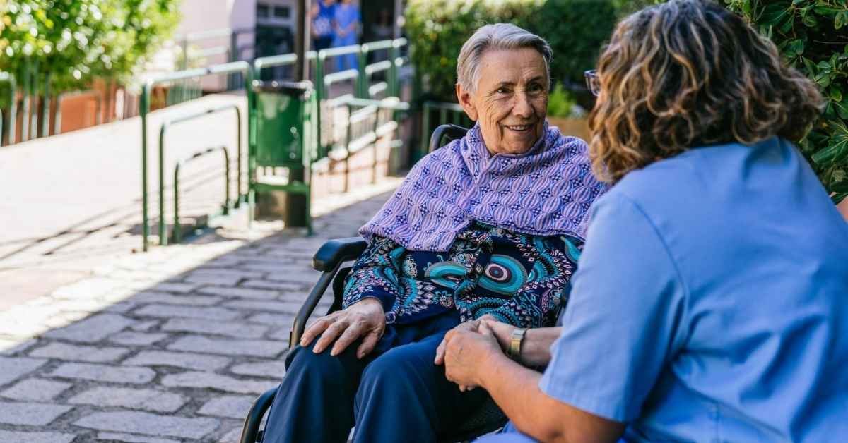 Senior woman in a wheelchair talking with a caregiver outdoors, illustrating how to hire a caregiver with compassion and trust.