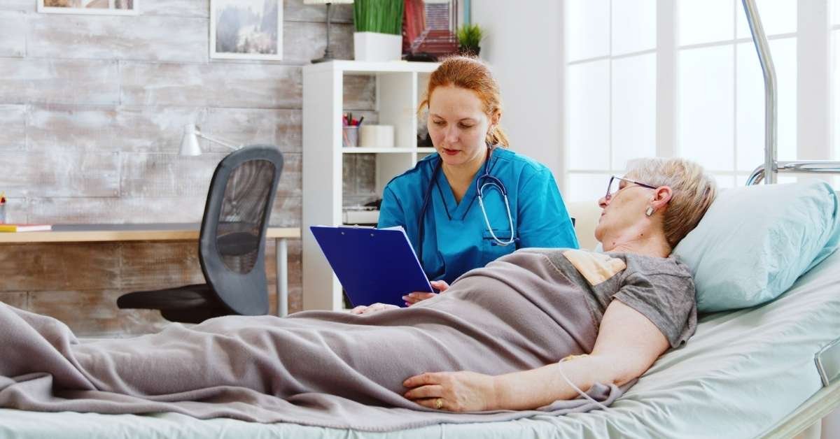 A nurse providing palliative care to a senior woman lying in bed, illustrating the difference between palliative care, hospice care, and home care in a home-like setting.