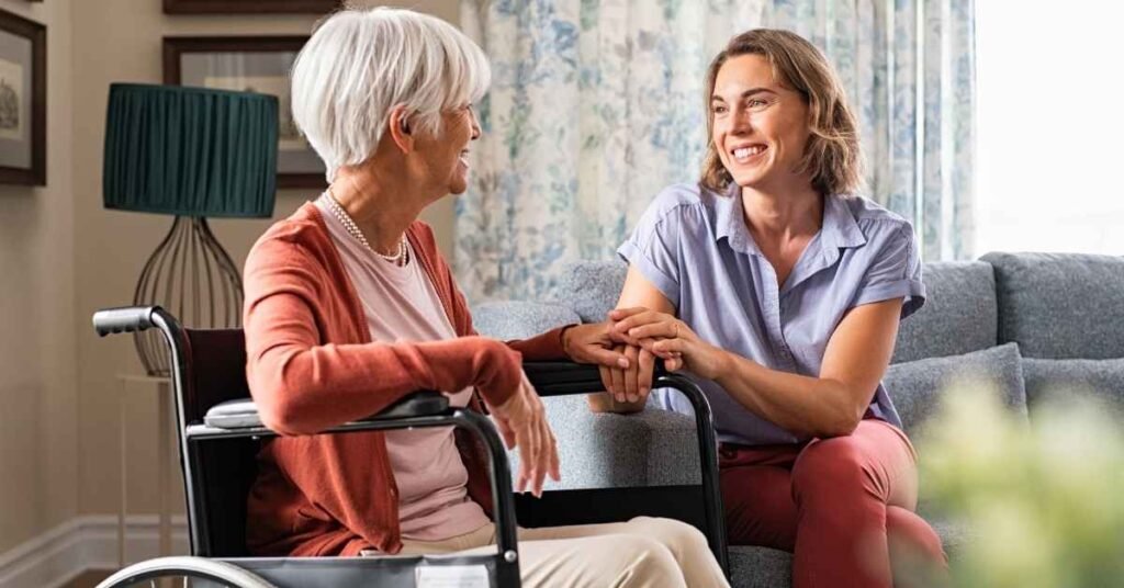 Family caregiver holding hands with her elderly mother in a wheelchair at home, showing compassion and support in the daily life of a family caregiver.