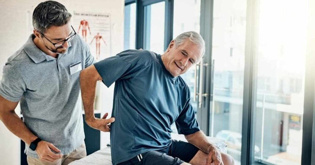 Senior man receiving physical support for back pain from a caregiver during in-home pain management support session.